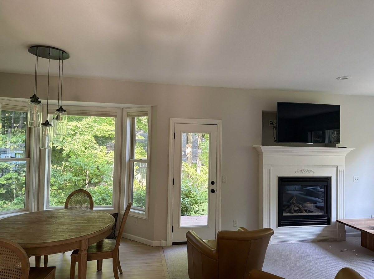 Great room before: beige walls, bay window, white traditional fireplace, carpet
